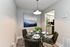Modern dining area with a stylish glass table set for four, complemented by elegant artwork and a sleek view into the contemporary kitchen.