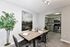Modern dining area with sleek wooden table, elegant place settings, and ambient lighting, leading to a stylish kitchen with stainless steel appliances.