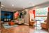 Chic lounge area with stylish seating, vibrant orange accents, and an inviting dining nook by a large window, perfect for relaxation or social gatherings.