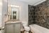 Modern bathroom with sleek granite countertop, chic cabinetry, and elegant gray tile bathtub surround.
