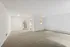 Spacious and bright living area with plush carpeting and elegant white walls, leading to a cozy kitchen and hallway.
