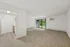 Spacious living area with plush carpet leading to a bright, open kitchen and large sliding glass doors opening to a lush green view.