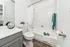 Modern bathroom with elegant white tiles, a sleek vanity, and stylish wood flooring, accented by colorful towels and greenery for a fresh and inviting atmosphere.