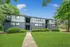 Charming apartment complex with modern blue siding, lush greenery, and a welcoming pathway.