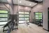 Modern gym space with natural light, featuring a variety of weights, kettlebells, and a sleek bench, surrounded by large windows with views of lush greenery.