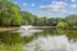 Serene lakeside apartment view with vibrant green trees and a charming water fountain creating a tranquil oasis.