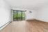 Bright living room with large sliding glass doors opening to scenic greenery, featuring elegant hardwood floors and modern white walls.