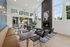 Elegant communal living space with high ceilings, modern fireplace, and large windows inviting natural light. Stylish seating offers comfort and a view towards a lush green exterior.