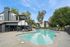 Inviting apartment complex with a sparkling pool, modern loungers, and lush greenery under a bright blue sky.