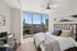 Chic bedroom with floor-to-ceiling windows offering stunning cityscape views, stylish decor, and cozy bedding.
