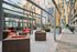 Modern outdoor lounge area with comfortable wicker furniture, vibrant red cushions, and elegant planters, surrounded by striking glass buildings.