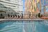 Luxurious outdoor pool area surrounded by modern skyscrapers, featuring elegant sun loungers and vibrant orange seating, perfect for relaxation in a sophisticated urban setting.