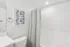 Sleek bathroom with modern design, featuring elegant gray shower curtain, abstract wall art, and pristine white fixtures.
