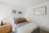 Cozy and elegant bedroom with stylish decor, featuring a plush bed with layered linens, accent pillows, bedside lamps, and modern artwork on the walls, creating a serene ambiance.