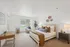 Bright and inviting bedroom with modern decor, large window, cozy bedding, and a stylish desk setup.