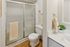 Modern bathroom with elegant glass shower door, stylish vanity with white countertop, and wood flooring accents.