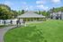 Serene apartment community featuring lush green lawns, a spacious clubhouse, and a sparkling pool under a clear blue sky.