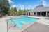 Inviting outdoor pool area with vibrant blue water, surrounded by elegant lounge chairs and lush greenery under a clear blue sky.