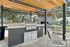 Elegant outdoor communal area with a sleek stainless steel barbecue grill under a stylish wooden pergola, featuring modern seating and a cozy fireplace, ideal for social gatherings.