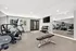 Modern fitness room with bright windows, equipped with exercise bike, treadmill, dumbbells, and a large mirror offering a spacious workout environment.
