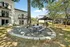 Charming apartment exterior with balconies overlooking a serene courtyard featuring a shaded picnic area under tall trees.