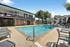 Inviting community pool area with modern lounge chairs, surrounded by elegant architecture and lush green trees.