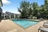 Inviting apartment complex with a sparkling outdoor pool, surrounded by lush greenery and modern seating, perfect for relaxation.