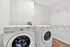 Sleek laundry room with modern front-loading washer and dryer, ample shelving space, and elegant hardwood floors.