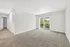 Bright, spacious living room in a modern apartment with plush carpet, natural light from large balcony doors, and serene views of greenery.