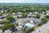 Charming aerial view of a modern apartment complex surrounded by lush greenery, featuring a refreshing swimming pool, ample parking, and vibrant community living.