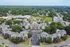 Charming aerial view of a modern apartment complex surrounded by lush greenery, showcasing convenient parking and nearby shopping amenities.