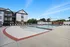 Beautiful apartment complex featuring a luxurious pool area with ample seating, modern buildings, and clear blue skies.