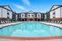 Inviting apartment complex boasting a large outdoor swimming pool with spacious sunbathing area, surrounded by stylish multi-story buildings.