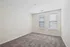 Bright, spacious empty room with clean carpet flooring and large double windows.