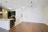 Elegant modern kitchen with granite countertops, dark wood cabinetry, and sleek stainless steel appliances, opening into a spacious living area with polished hardwood floors.