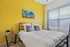 Bright and inviting bedroom with a vibrant yellow accent wall, stylish metal bedframe, and natural light streaming through large windows.