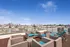 Chic rooftop terrace with stylish furniture offering panoramic city skyline views under a clear blue sky.