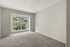 Bright and inviting room with plush carpet flooring and a large window overlooking lush greenery, perfect for relaxation.