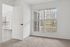 Bright bedroom with plush carpet and large windows offering scenic views, leading into a spacious room with elegant flooring.