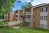 Inviting brick apartment complex surrounded by lush greenery, featuring spacious balconies and a serene walkway.