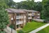 Charming brick apartment building nestled in lush greenery, featuring private balconies and a welcoming entrance walkway.
