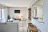 Inviting living room with modern decor, cozy furniture, and a wall-mounted TV, complemented by a sleek open-concept kitchen and natural light from sliding glass doors.