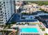 Aerial view of a modern apartment complex featuring a sparkling swimming pool, comfortable lounge areas, and lush greenery, set against a backdrop of urban architecture and vibrant cityscape.