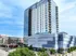 Contemporary high-rise apartment building with sleek glass facade and spacious balconies, located above vibrant retail spaces in a bustling urban setting.