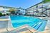 Inviting apartment complex with a sparkling outdoor pool, modern lounge chairs, and lush greenery under a clear blue sky.