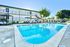 Inviting apartment complex featuring a crystal-clear swimming pool, poolside lounge chairs, and vibrant green trees under a clear blue sky.