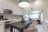 Chic open-plan kitchen and dining area with elegant light fixtures and modern seating, seamlessly leading to a stylish living room filled with natural light.