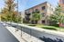 Modern brick apartment complex with balconies, surrounded by lush trees and clean sidewalks, offering a peaceful residential environment.