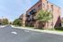 Charming brick apartment building with private balconies, surrounded by lush greenery and a quiet street, perfect for modern living.
