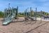 Inviting playground area featuring modern climbing equipment and slides, surrounded by lush greenery and a clear blue sky.